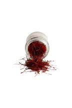 Red saffron threads spilling from a small clear glass jar on a white background.