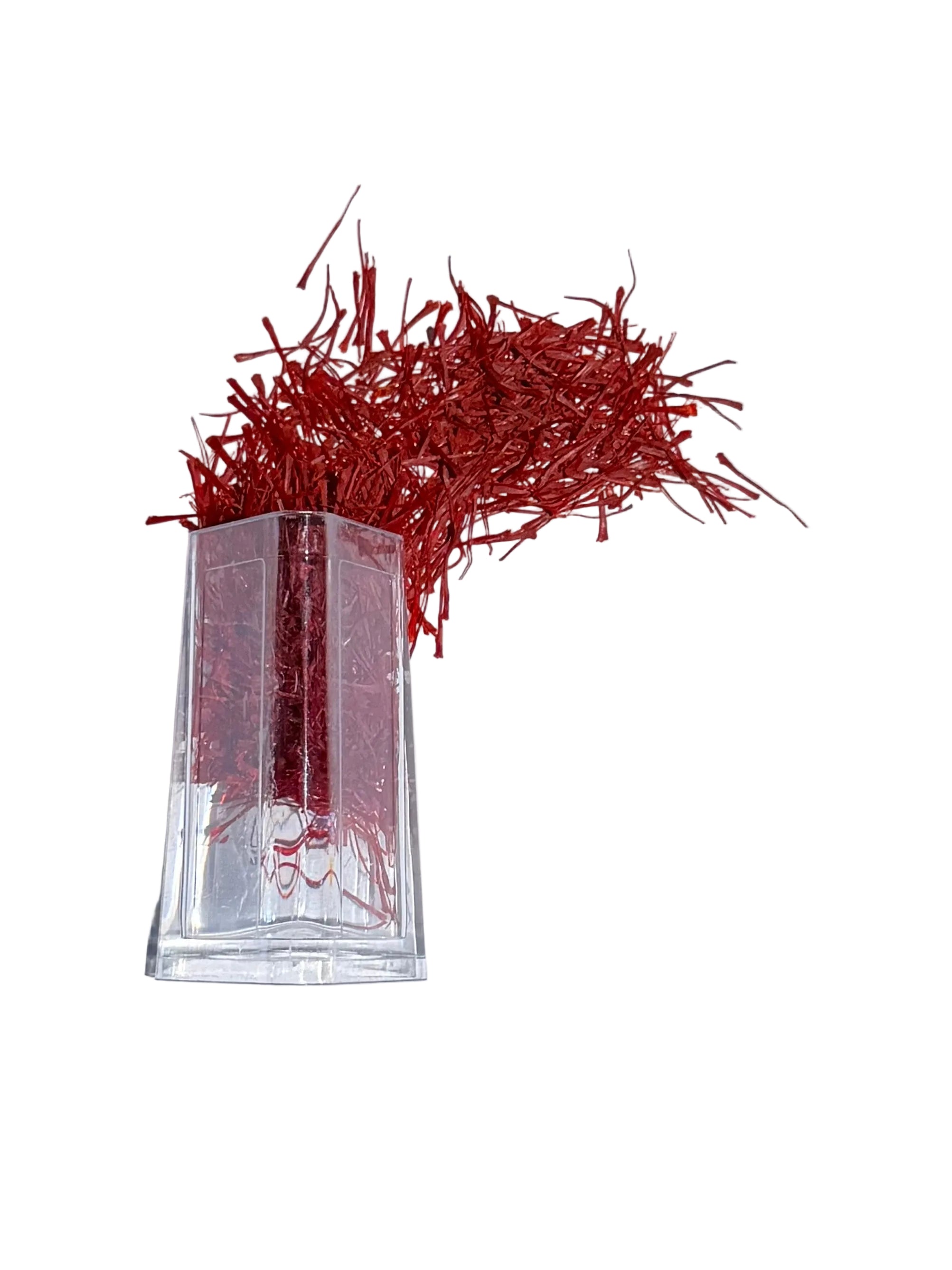 A small clear glass vial filled with red liquid or fibers, placed on top of a white sheet of paper on a beige floor. A dark shadow covers the lower-left portion of the photo, and part of a patterned rug is visible in the upper-left corner.