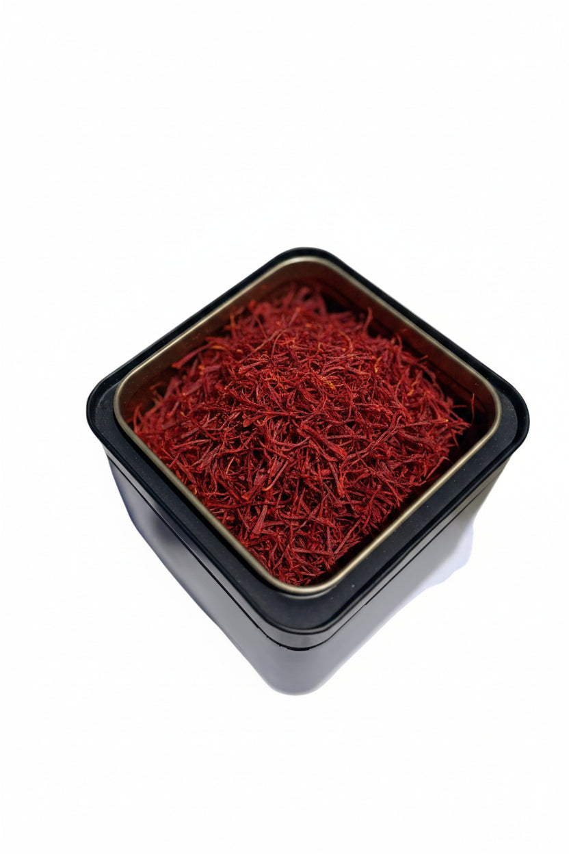 A square black metal tin filled with loose red powder, photographed from above on a white sheet of paper over a light beige surface.